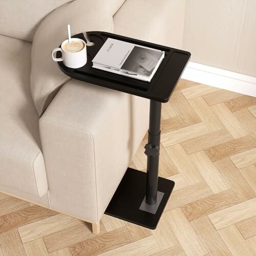 Adjustable side table with coffee and book beside a couch.