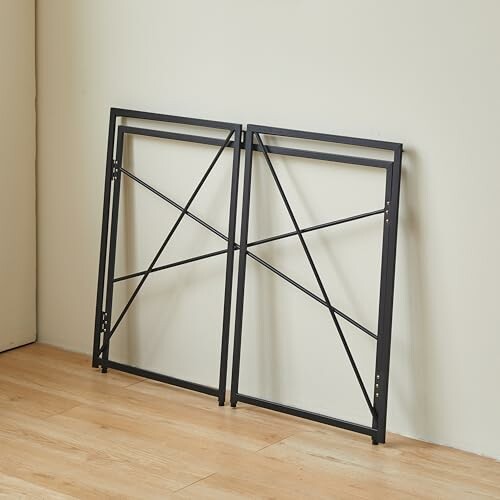 Two black foldable table legs against a wall.