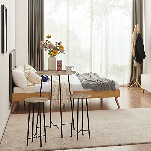 Modern bedroom with a tall table and stools beside a bed.