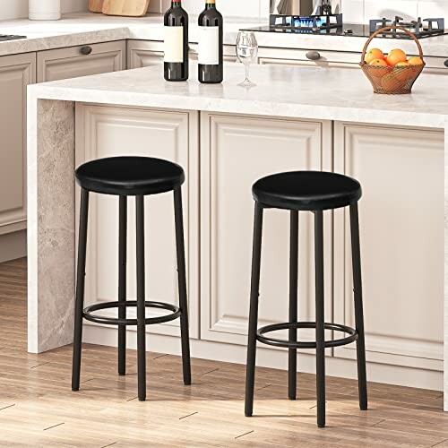 Two black bar stools in a kitchen with a white countertop and a fruit basket.